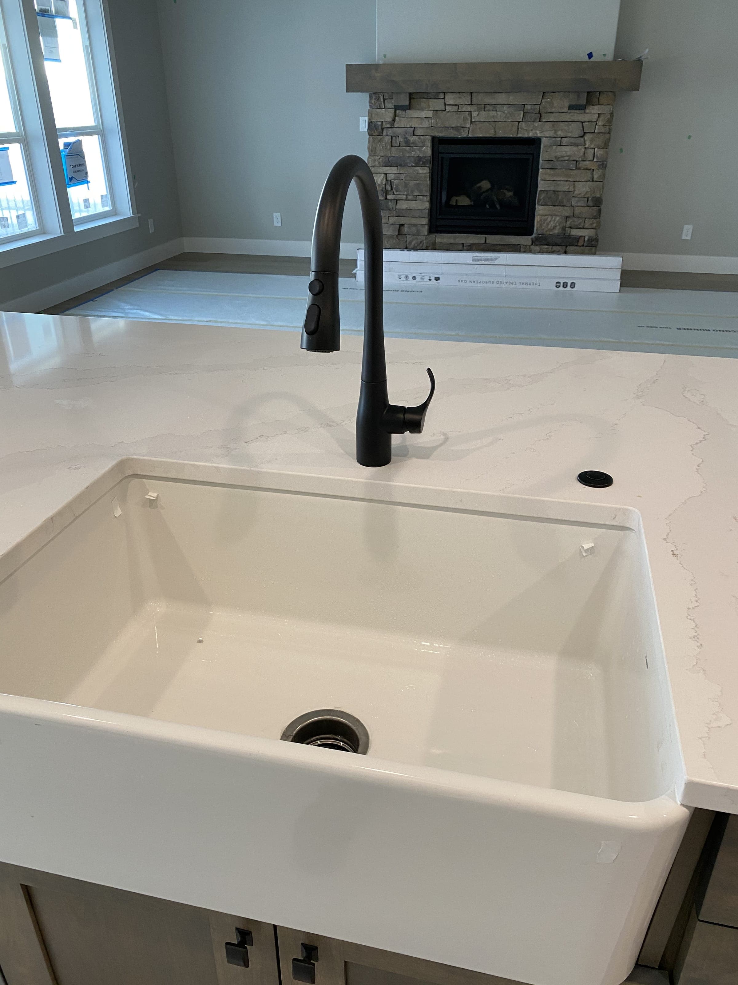 A newly installed farmhouse sink and black pull-down kitchen faucet on a quartz worktop
